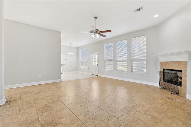 unfurnished living room featuring ceiling fan with notable chandelier and a tiled fireplace