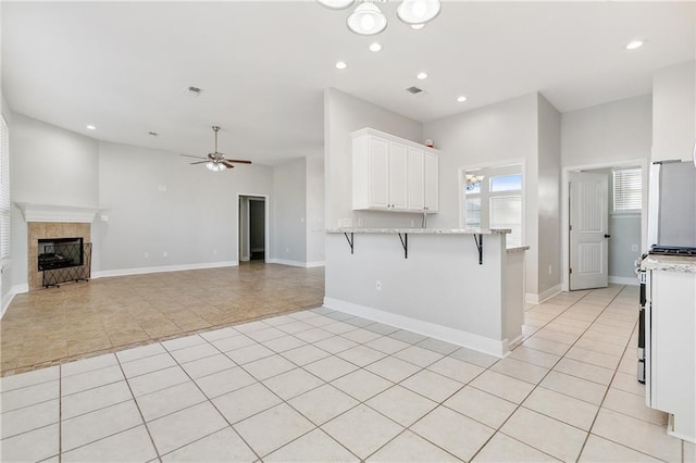 kitchen with white cabinets, white refrigerator, ceiling fan, light stone countertops, and a kitchen bar