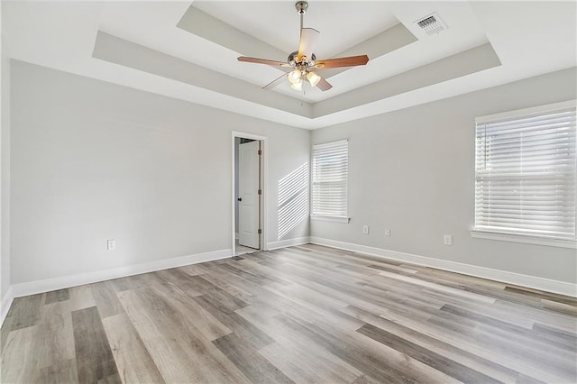 spare room featuring light hardwood / wood-style floors, a raised ceiling, ceiling fan, and a healthy amount of sunlight