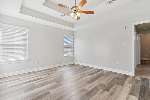 empty room with ceiling fan, light hardwood / wood-style floors, and a tray ceiling