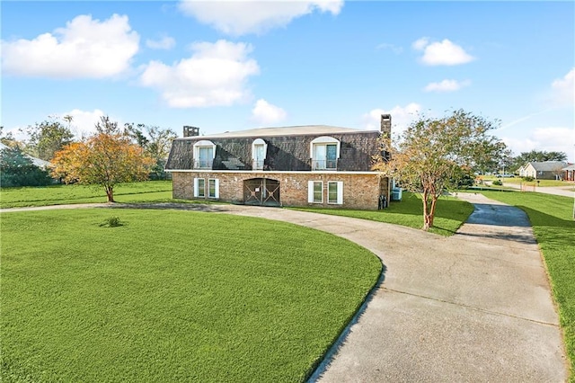 view of front facade with curved driveway, a front lawn, mansard roof, and brick siding