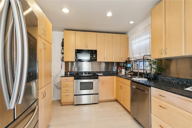 kitchen featuring sink, light brown cabinetry, dark stone counters, and appliances with stainless steel finishes