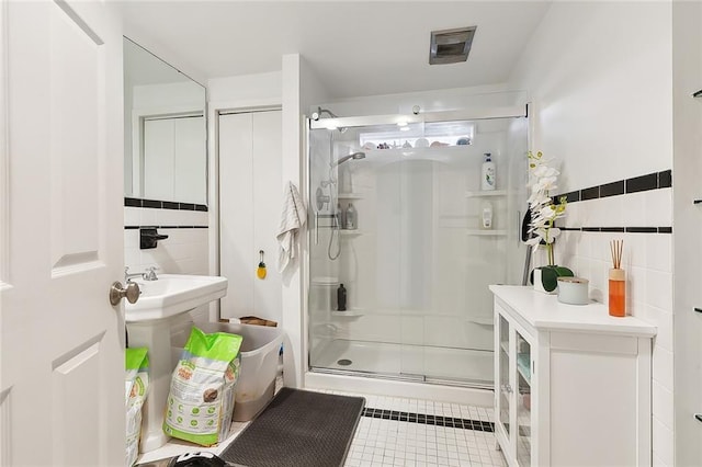 bathroom featuring tile patterned floors, sink, a shower with shower door, and tile walls