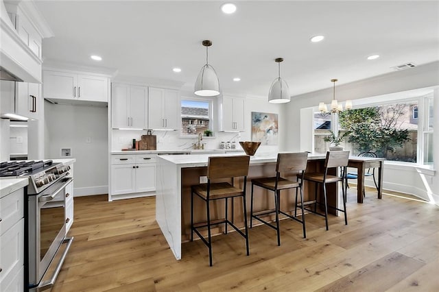 kitchen featuring pendant lighting, stainless steel range with gas cooktop, a center island, and light hardwood / wood-style floors