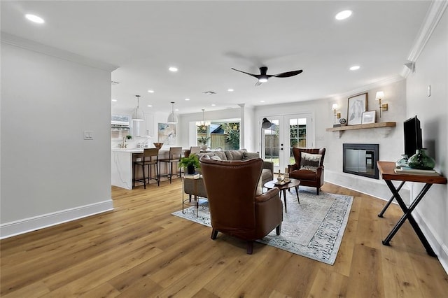 living room with ceiling fan with notable chandelier, light hardwood / wood-style floors, ornamental molding, and french doors