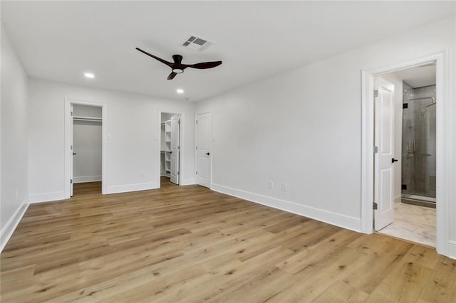 unfurnished bedroom featuring a walk in closet, light hardwood / wood-style floors, ensuite bath, and ceiling fan