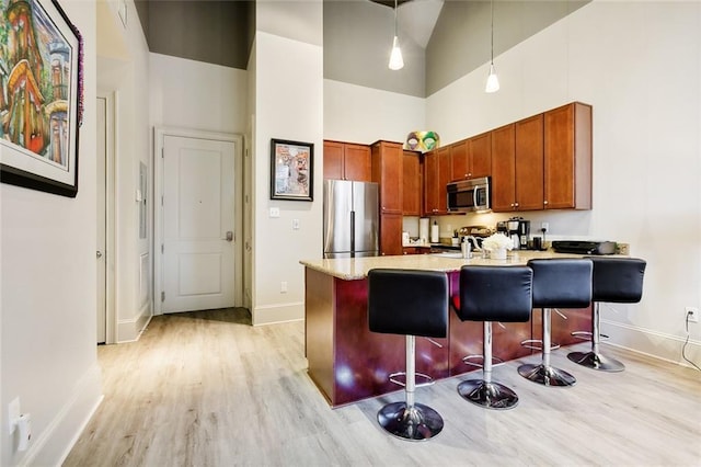 kitchen featuring high vaulted ceiling, hanging light fixtures, light hardwood / wood-style flooring, a kitchen bar, and stainless steel appliances