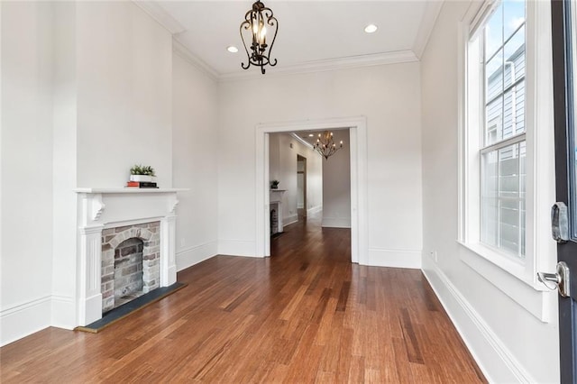 unfurnished living room featuring dark hardwood / wood-style flooring, a stone fireplace, crown molding, and a chandelier