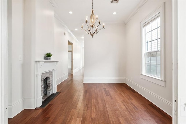 unfurnished living room featuring hardwood / wood-style floors, an inviting chandelier, crown molding, and a brick fireplace