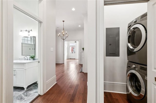 laundry room with dark wood-type flooring, electric panel, an inviting chandelier, crown molding, and stacked washer / dryer