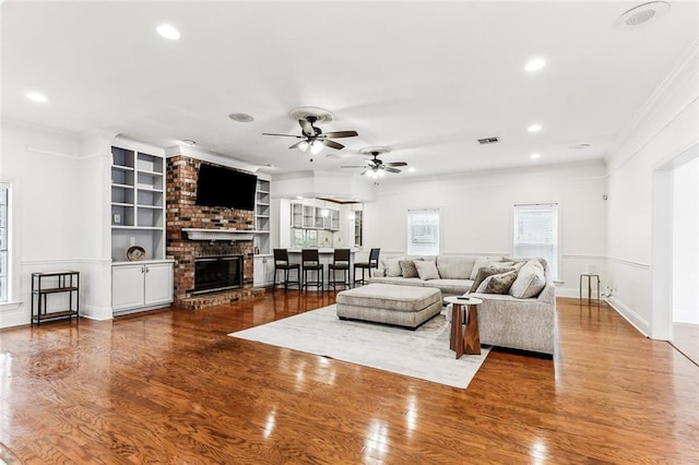 living room featuring crown molding, ceiling fan, a brick fireplace, dark hardwood / wood-style floors, and built in shelves