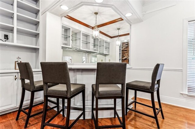 bar featuring ornamental molding, white cabinets, decorative light fixtures, and hardwood / wood-style flooring