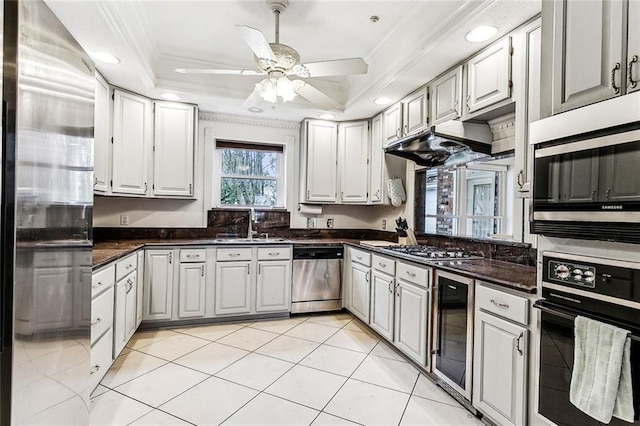 kitchen featuring a raised ceiling, wine cooler, appliances with stainless steel finishes, ornamental molding, and white cabinetry