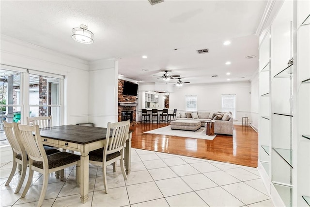 tiled dining room featuring ceiling fan, crown molding, and a fireplace