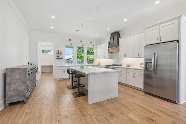 kitchen featuring white cabinetry, a breakfast bar, custom range hood, and stainless steel refrigerator with ice dispenser