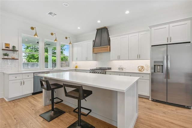 kitchen featuring white cabinets, premium range hood, appliances with stainless steel finishes, and a kitchen bar