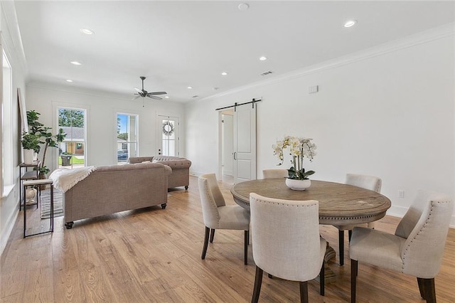 dining area featuring ceiling fan, a barn door, light wood-type flooring, and crown molding