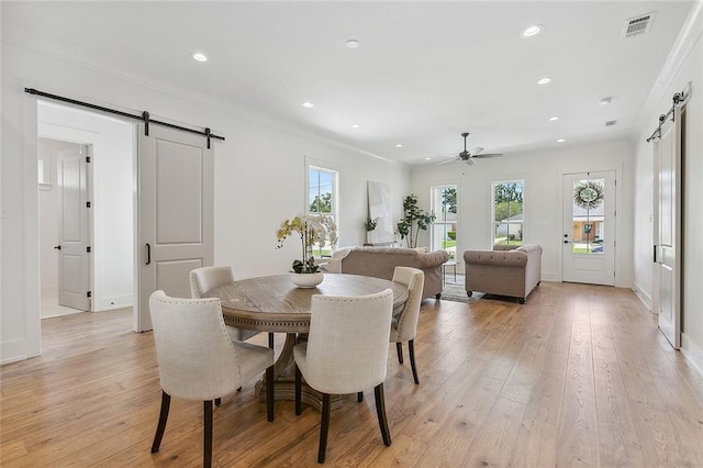 dining room with light wood-type flooring, a barn door, and ornamental molding