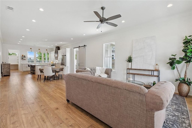 living room with light hardwood / wood-style floors, crown molding, a barn door, and ceiling fan