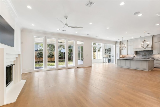 unfurnished living room featuring ceiling fan with notable chandelier, light hardwood / wood-style floors, and crown molding