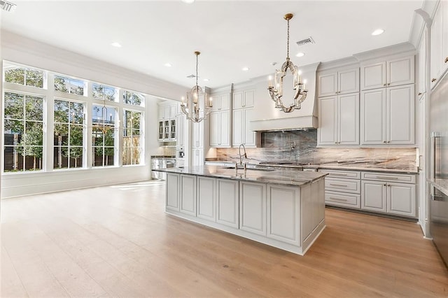 kitchen featuring sink, an island with sink, decorative light fixtures, and light wood-type flooring