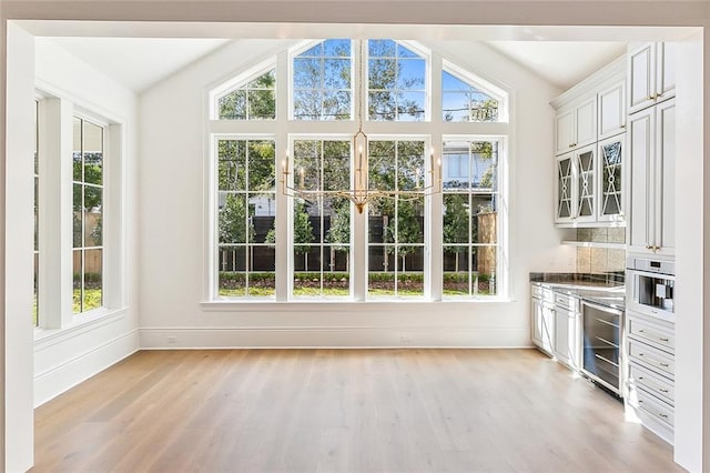 interior space with light hardwood / wood-style floors, white cabinetry, wine cooler, and vaulted ceiling