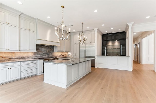 kitchen with light hardwood / wood-style flooring, dark stone countertops, decorative light fixtures, a kitchen island with sink, and custom range hood