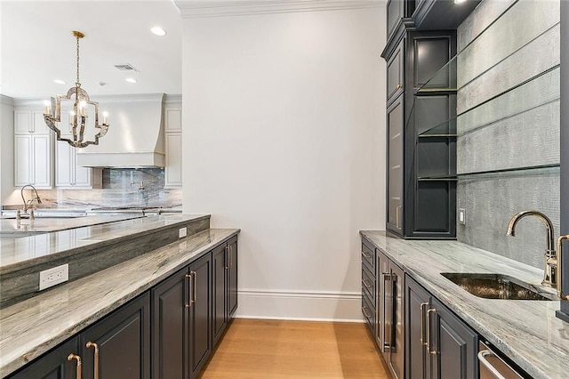 bar with light stone countertops, sink, tasteful backsplash, light hardwood / wood-style flooring, and custom exhaust hood