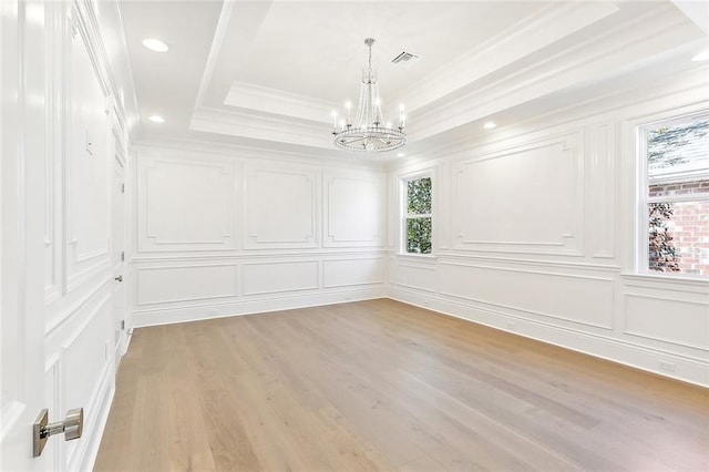 spare room with an inviting chandelier, a raised ceiling, crown molding, and light hardwood / wood-style flooring