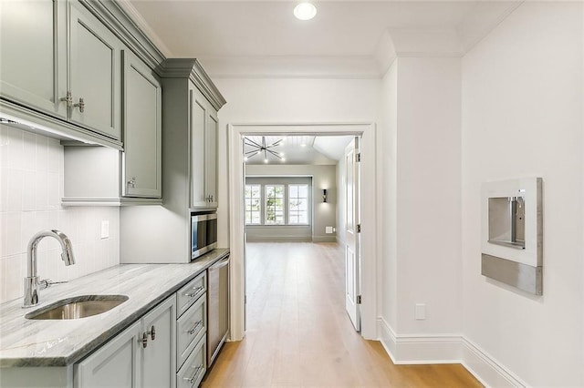 kitchen with light stone countertops, light wood-type flooring, tasteful backsplash, crown molding, and sink