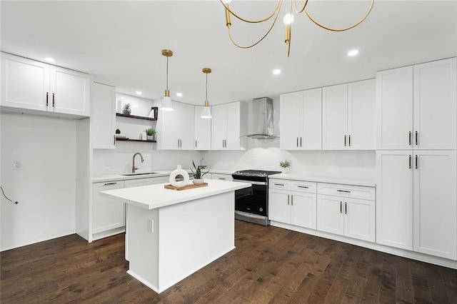 kitchen featuring white cabinets, wall chimney range hood, sink, stainless steel stove, and decorative light fixtures