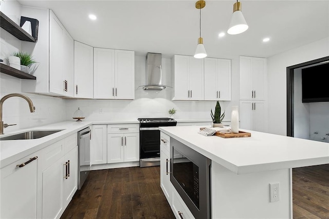 kitchen featuring wall chimney range hood, hanging light fixtures, sink, appliances with stainless steel finishes, and white cabinetry