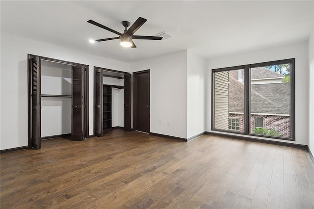 unfurnished bedroom with ceiling fan, dark wood-type flooring, and two closets