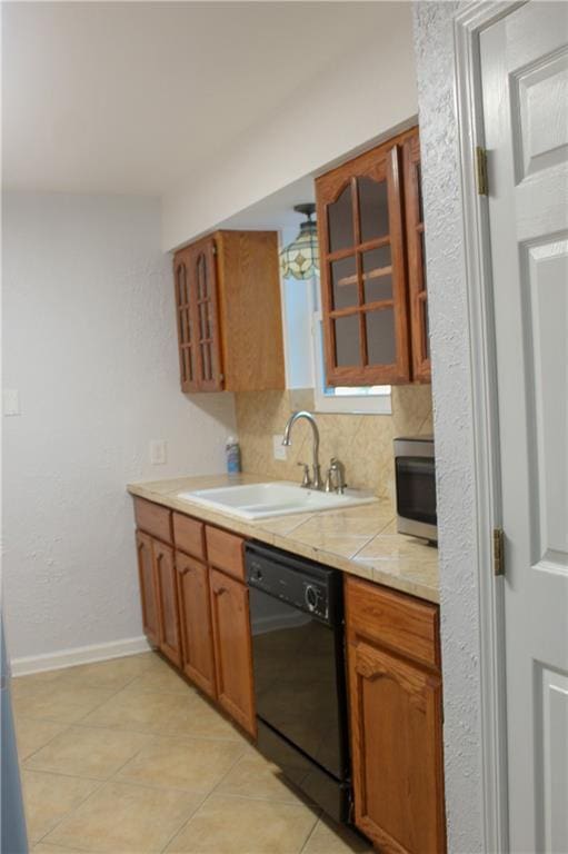 kitchen featuring tasteful backsplash, sink, light tile patterned floors, tile countertops, and black dishwasher