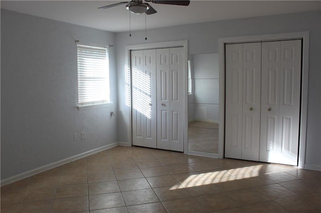 unfurnished bedroom with ceiling fan, light tile patterned floors, and multiple closets