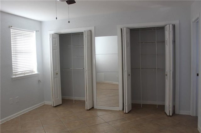 unfurnished bedroom with light tile patterned floors, two closets, and ceiling fan