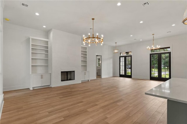 unfurnished living room featuring a fireplace, french doors, light hardwood / wood-style floors, and a chandelier