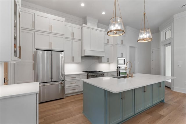 kitchen with appliances with stainless steel finishes, light wood-type flooring, decorative light fixtures, and a center island with sink