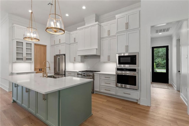 kitchen featuring high end appliances, light wood-type flooring, a kitchen island with sink, and hanging light fixtures