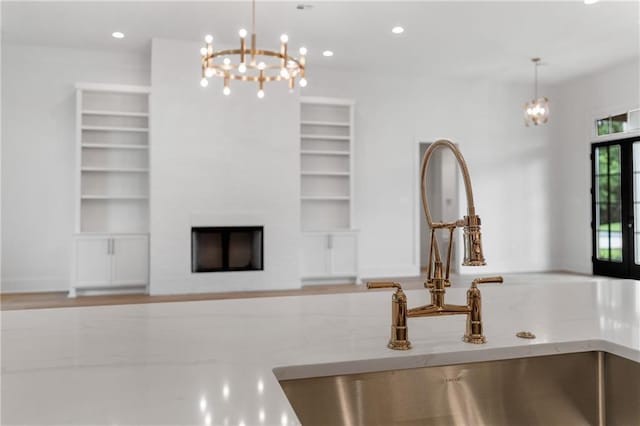 unfurnished living room featuring a fireplace, sink, french doors, and a notable chandelier