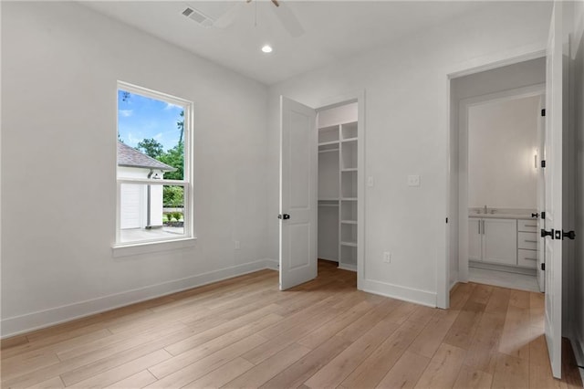 unfurnished bedroom with ceiling fan, light hardwood / wood-style floors, a walk in closet, and sink