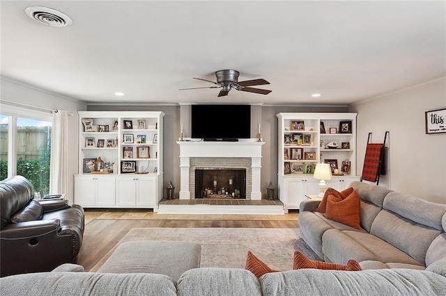 living room with ceiling fan, light wood-type flooring, a fireplace, and ornamental molding