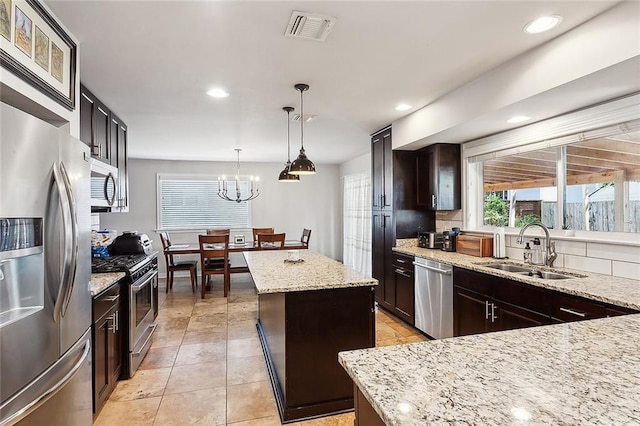 kitchen featuring appliances with stainless steel finishes, light stone counters, sink, pendant lighting, and a kitchen island