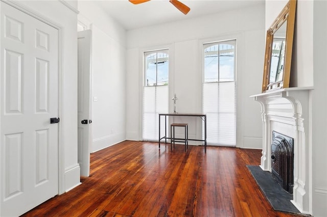 unfurnished living room featuring wood-type flooring, a fireplace with flush hearth, baseboards, and ceiling fan