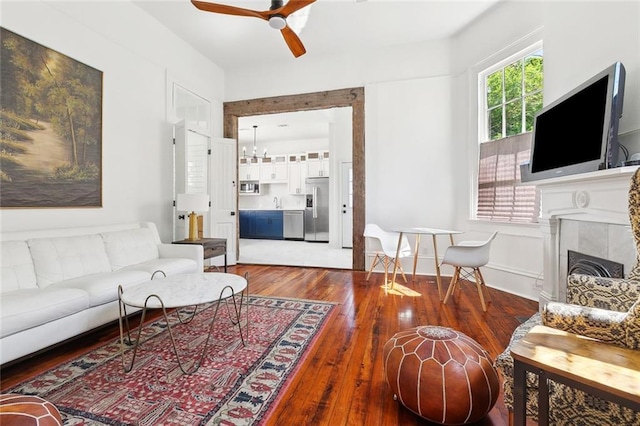 living area with hardwood / wood-style floors, a tiled fireplace, and a ceiling fan