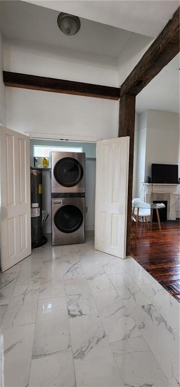 clothes washing area featuring water heater, light hardwood / wood-style flooring, and stacked washer and clothes dryer