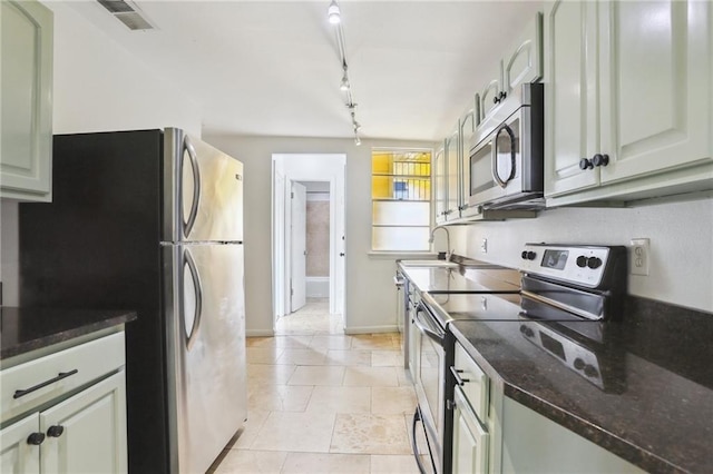 kitchen with appliances with stainless steel finishes, rail lighting, dark stone counters, sink, and light tile patterned floors