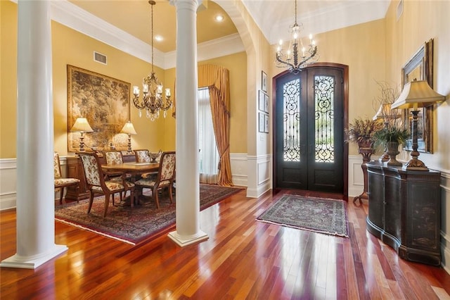 entrance foyer featuring french doors, ornate columns, ornamental molding, hardwood / wood-style flooring, and a chandelier