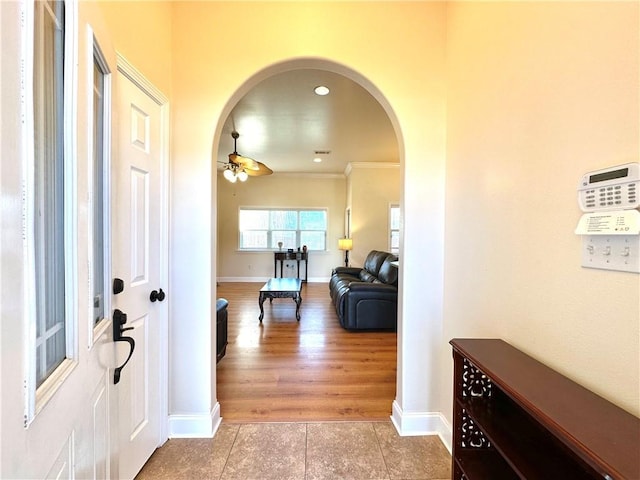 entrance foyer featuring baseboards, arched walkways, ceiling fan, light wood-style floors, and crown molding