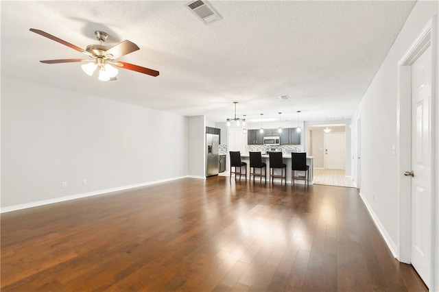 unfurnished living room featuring a textured ceiling, dark hardwood / wood-style floors, and ceiling fan with notable chandelier